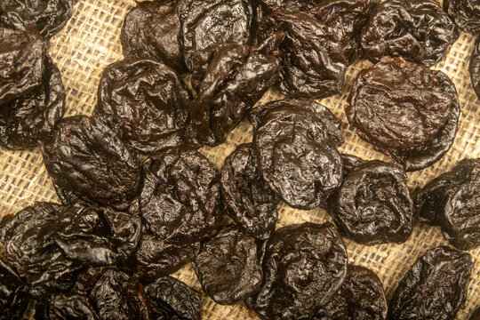 Dried prunes in bulk on burlap with a rough texture. Close up.