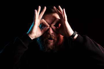 a photograph in the dark key of a manly which folded his fingers in the form of glasses and looks...