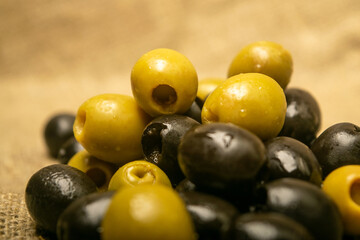 Green olives and black olives scattered on sacking with rough texture. Close up.