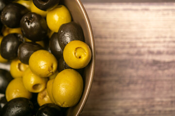Green olives and black olives in a ceramic bowl on a wooden background. Close up.