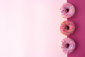 three donuts with glaze on a pink background, top view