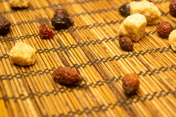 Pieces of brown cane sugar and dried rosehip fruit scattered on a reed Mat. Close up.