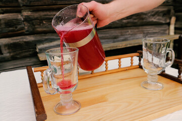 Male hand pours berry compote into a glass. Raspberry, currant or strawberry mors in a glass jug on a rustic background and two glasses. © d_odin