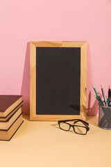 Chalkboard, books, glasses and pens on a yellow pink background. Concept to teacher's day. Copy space.