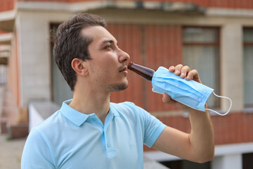 Man enjoys drinking an alcoholic drink in the city. A mask dressed on a bottle does not formally...