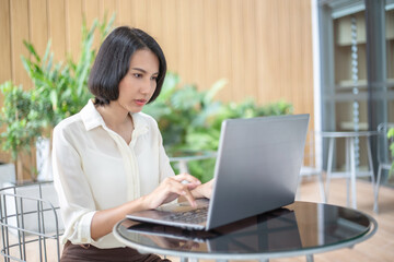 Young Asian woman using laptop computer and tablet PC to working in the modern co working space	