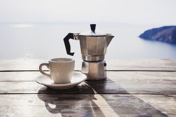 Italy travel, cup of coffee and moka machine coffee maker on a table over blue sky and sea. Summer...