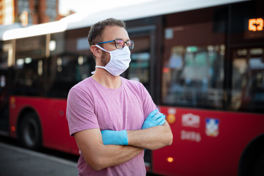 Man with medical protective mask and gloves waiting for the bus on a public transportation station.