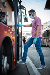 Man with medical protective mask and gloves entering the bus on a public transportation station.