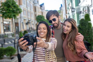 Girl with dreadlocks taking selfie on camera with friends in city.