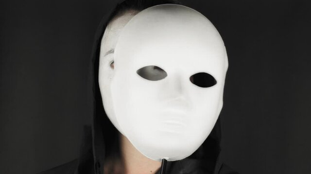 Brunette woman with white theatrical mask and make-up on her face. Sad girl takes off the theatrical mask from her face and looks at the camera. Hide emotions. 