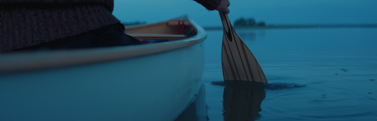 CU view of a paddle, man canoeing alone boat on a large lake at dawn