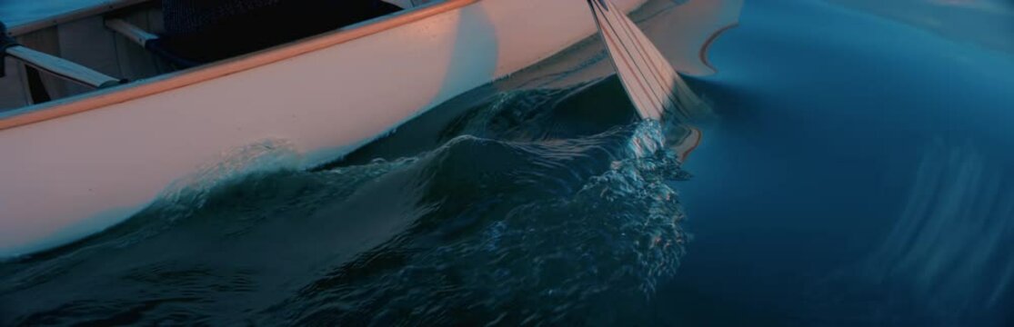 CU view of a paddle, man canoeing alone boat on a large lake at dawn. Shot on RED cinema camera with 2x anamorphic lens