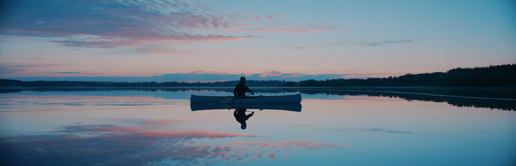 Man canoeing in a traditional wooden boat on a large lake at dawn