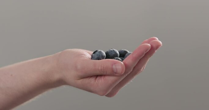 Slow motion man hand show big ripe blueberries on neutral background
