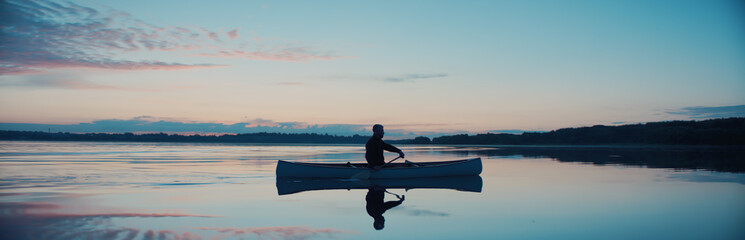 Man canoeing in a traditional wooden boat on a large lake at dawn