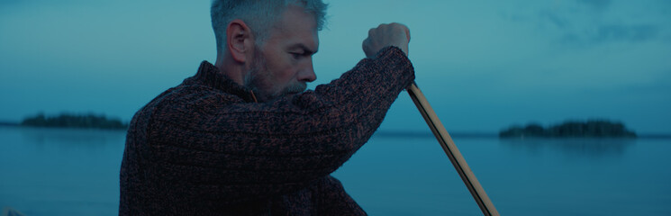 Portrait of mid 50s man canoeing alone boat on a large lake at dawn