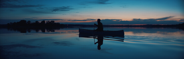 Man canoeing in a traditional wooden boat on a large lake at dawn