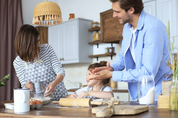 Cute little girl and her parents are having fun while cooking in kitchen at home together.