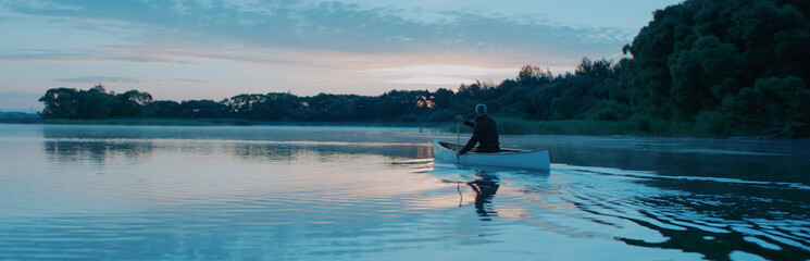 Man canoeing in a traditional wooden boat on a large lake at dawn