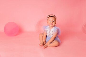 Happy kid girl with balloons on a pink background celebrates her first birthday