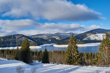 Winter landscape from the mountain with lake, fir forest, snow and blue sky with clouds
