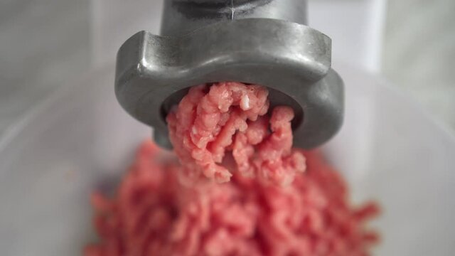 Electric mincer machine closeup. Filling comes out through meat grinder sieve. Grinder with fresh chopped meat. Process of raw meat grinding in kitchen with mincing machine. Preparation of minced beef