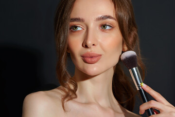 Portrait of the beautiful brunette woman with make-up brushes near face. Girl posing over Gray background. Clean natural makeup.