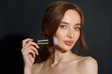 Portrait of the beautiful brunette woman with make-up brushes near face. Girl posing over Gray background. Clean natural makeup.