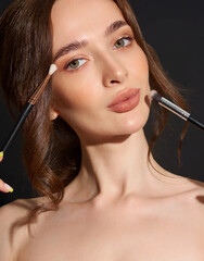 Portrait of the beautiful brunette woman with make-up brushes near face. Girl posing over Gray background. Clean natural makeup.