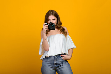 Young female photographer with camera over yellow background