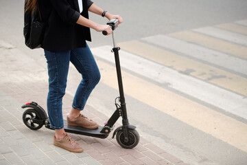Low section of young female with electric scooter standing by crosswalk on road