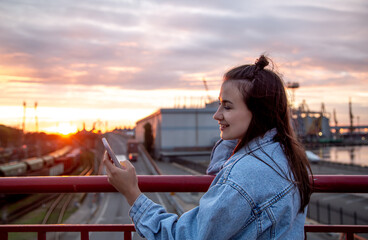 Obraz premium A young woman photographs a beautiful sunset from a bridge.