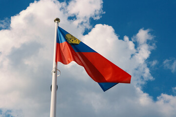 Flag of Liechtenstein evolving in the wind against the background of the summer sky with white clouds.