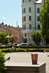 Fototapeta na wymiar Brown paper cup on a background of urban architecture. Coffee on a marble border. The houses of the old town are blurred in the background. Sharpness on coffee. Layout for design.
