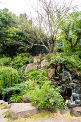 Glover Garden in Nagasaki, Japan, with green plants and trees formations on the rock, small waterfall, portrait view.