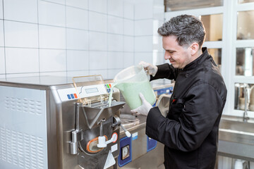 Chef pouring mixed milk base into the ice cream machine or freezer at the small ice cream manufacturing or restaurant kitchen