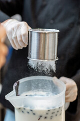 Chef sprinkling powdered sugar on the milk base with blue berries, making ice cream, close-up