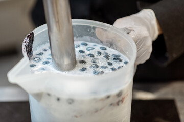 Chef blending milk with blueberries, preparing base for ice cream production, close-up