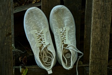 two white shoes made of fabric stand on brown wooden planks wall outdoors
