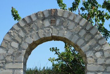 part of the architectural structure of a gray brick arch on a background of blue sky and green tree...