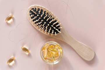 Hair loss concept. Comb with hair and supplement on light pink background. Flat lay. Close up. 