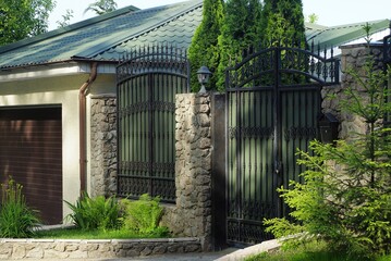 green metal gate with a black forged pattern and part of the fence wall of gray stones on the street