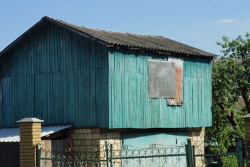 attic of a blue rural wooden house with a boarded up window against the sky