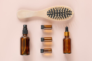 Hair loss concept. Comb with hair, emulsions and essential oils on light pink background. Flat lay. Knolling.
