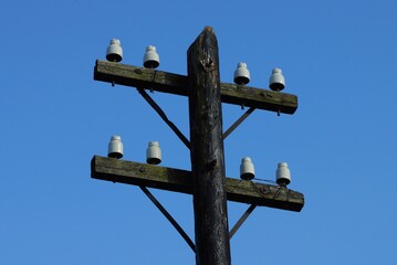 one black old wooden electric pole without wires against a blue sky