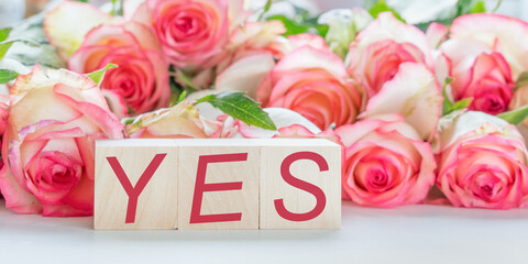 sign and text yes written on wooden blocks love and wedding concept bouquet of roses flowers background