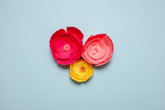 Paper art and craft handmade flowers. Pink and yellow colors. On blue background.
