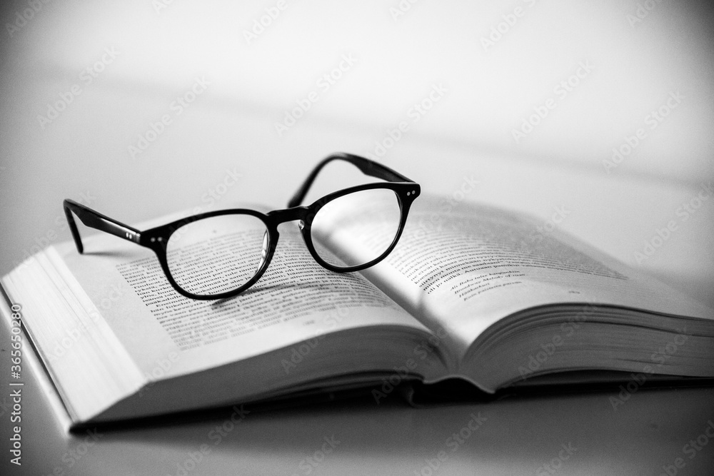Poster grayscale shot of a pair of glasses on an open book with a white background