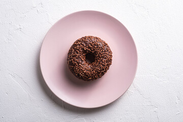 Chocolate donut with sprinkles on pink plate, sweet glazed dessert food on white concrete textured...